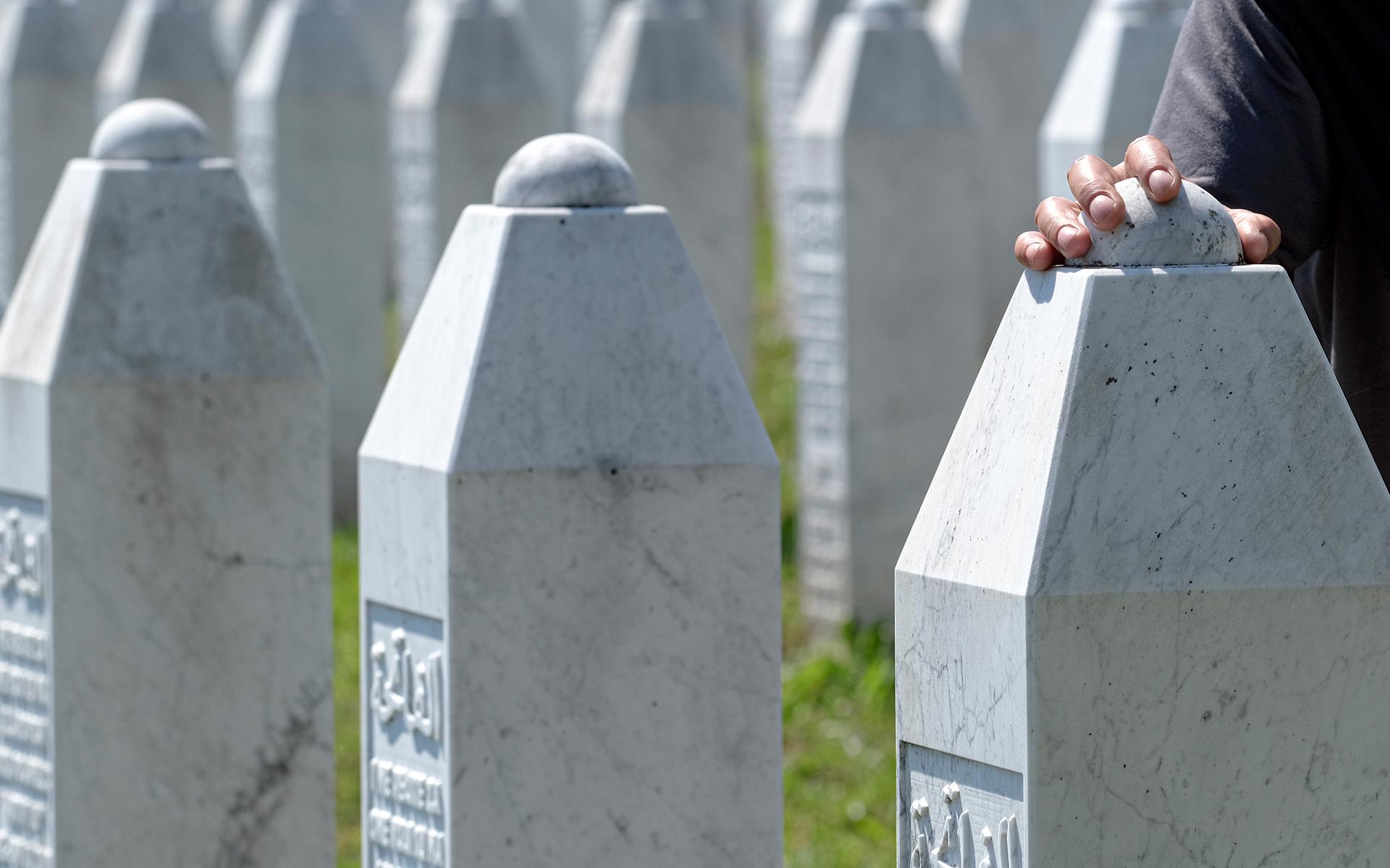 En kvinna vidrör en gravsten i Potocari, nära Srebrenica, Bosnien, lördagen den 11 juli 2020. I år är det 27 år sedan folkmordet ägde rum. 