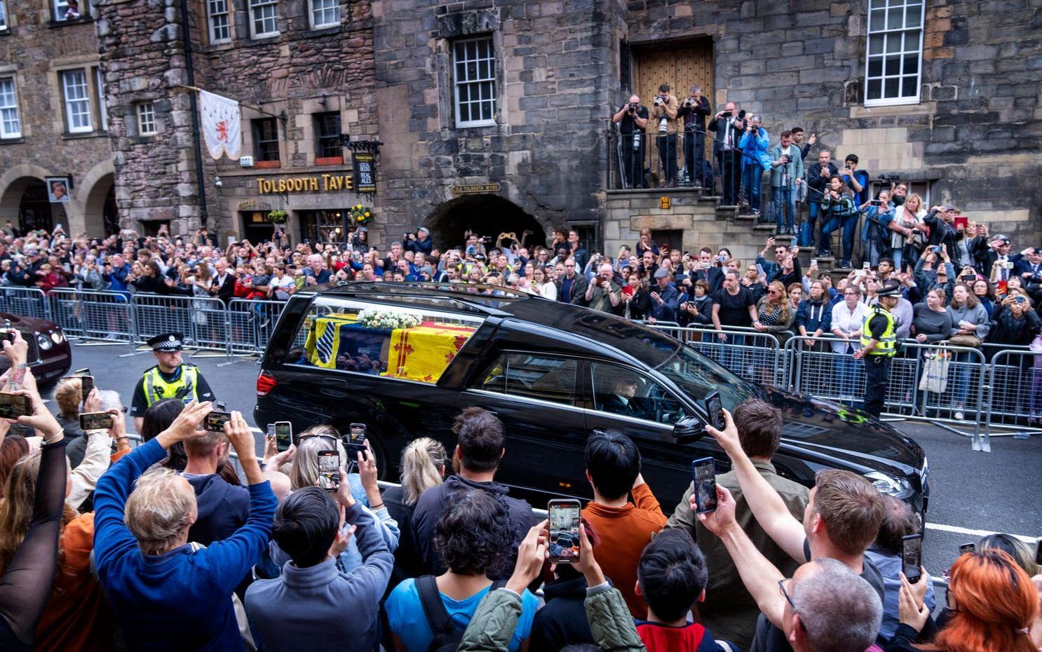 Åskådare och fotografer har trängt sig upp längs med husfasaderna för att kunna fånga en glimt av drottning Elizabeth II kista när den färdas genom Edinburgh.