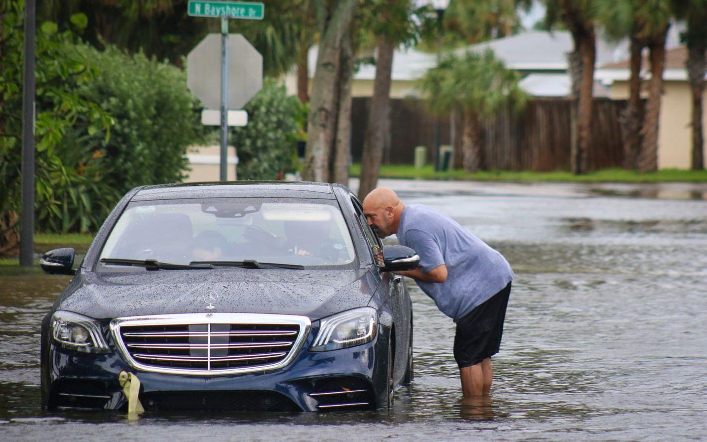 En man försöker hjälpa en person som har fastnat med bilen i vattenmassorna i Madeira Beach, Florida. 