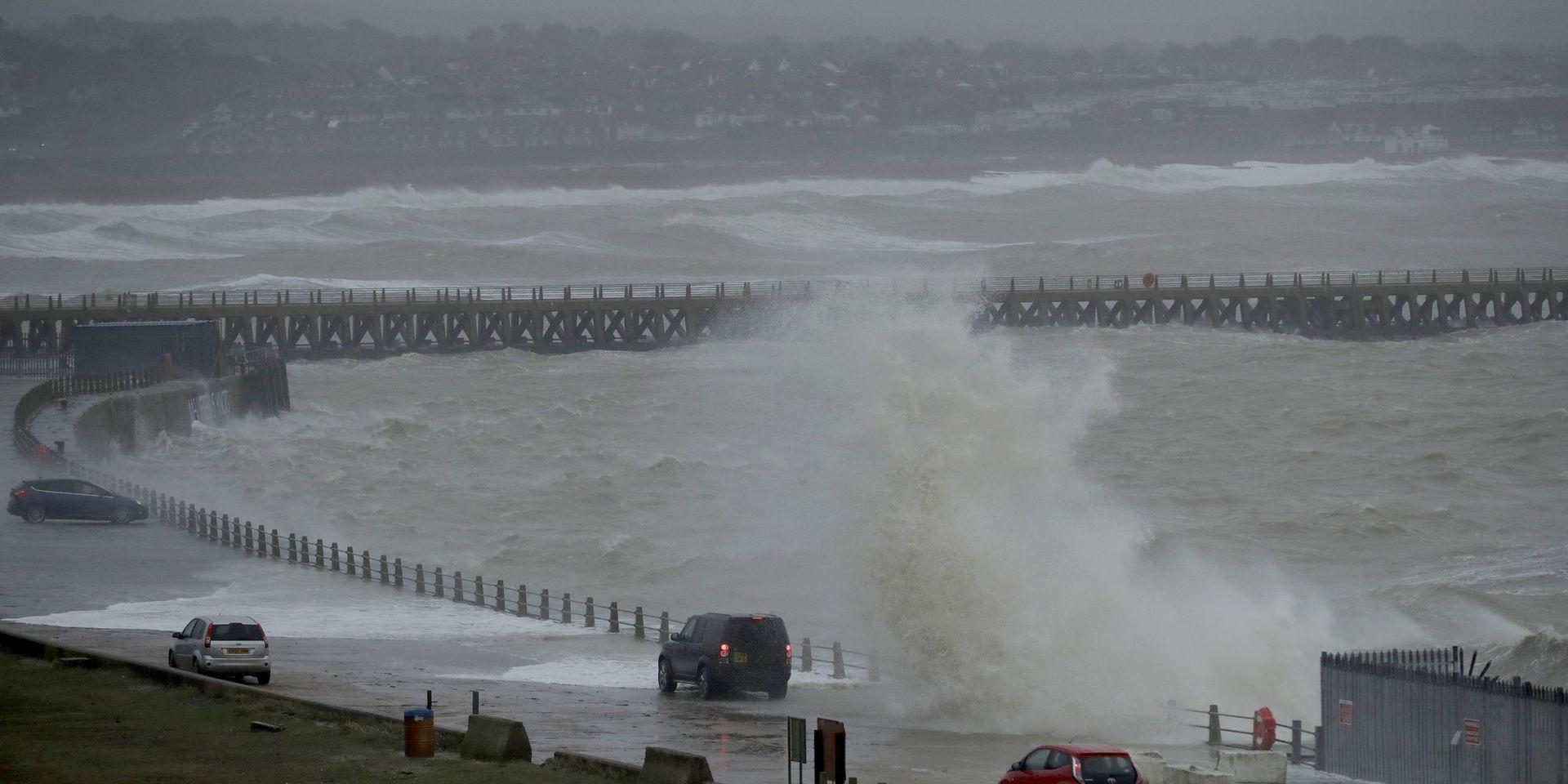 En våg slår över vägen medan bilar i sakta mak tar sig fram i Newhaven på Englands södra kust. Bild tagen 9 februari. 