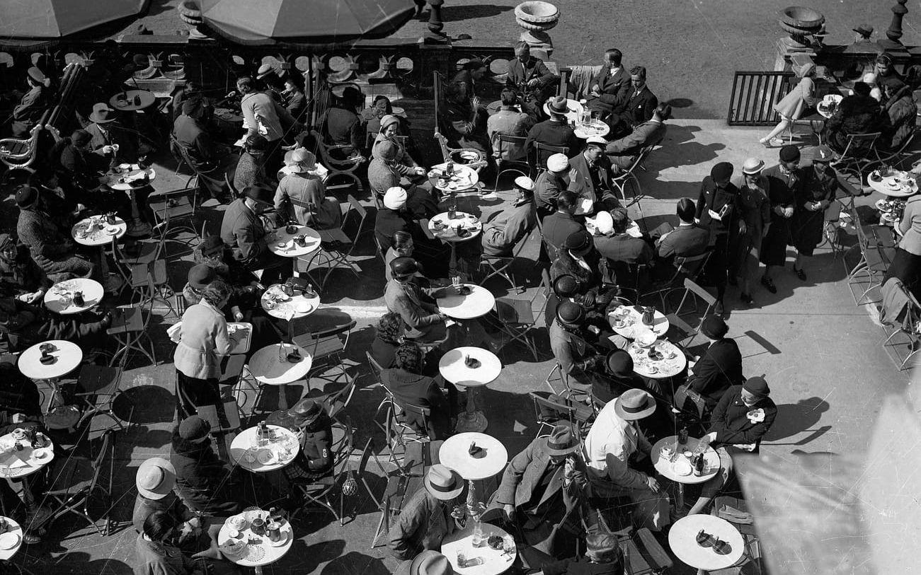 Fullsatt – nästan – på Trädgårdsföreningen kafé den 7 maj 1935. De runda arrangemangen på varje bord är askfat. Nästan ingen är barhuvad. Studenterna bär vita mössor.  Trädgårdsföreningen i Göteborg är en av Sveriges äldsta offentliga parker – grundad år 1842, samma år som hjulångarna började gå mellan Göteborg och London. Anton Franz Töpel, en trädgårdsmästare från Saxen, värvades till Göteborg för att bygga parken. Om honom skrev sedermera Viktor Rydberg i Göteborgs- Handel- och Sjöfarts-Tidning: ”Han bidrog till parkens anläggning, väl icke med penningen, men med det skapande skönhetssinnets högre makt”. Töpel behövde i verkligheten all tänkbar tillgång till både penningar och högre makter, för Trädgårdsföreningen visade sig ligga på ren lera. Det var besvärligt de första decennierna. Restaurangen öppnade 1887. Sedan dess har det – i princip, med små variationer i modet och i glasen  – sett ut ungefär som på fotografiet. 